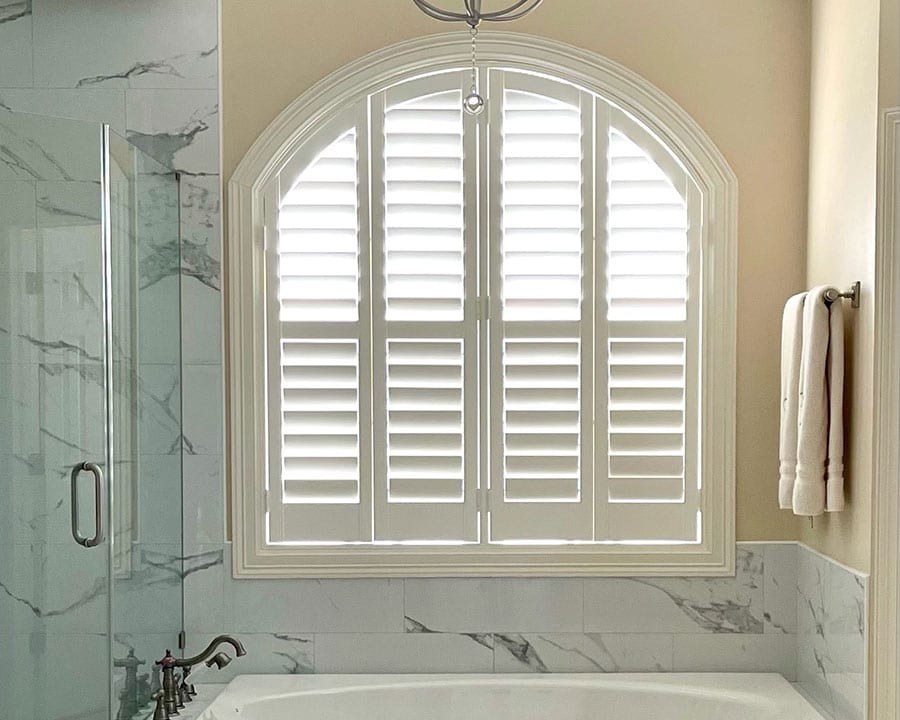 white marble glass shower and sunken tub facing white plantation shutters in Houston TX