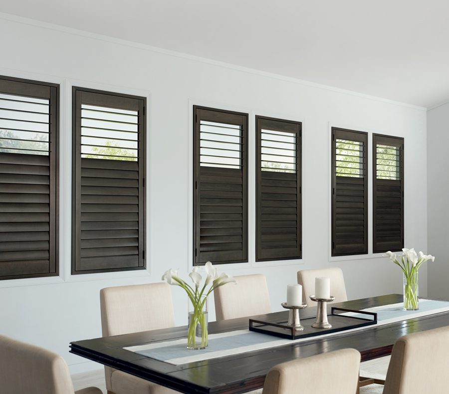 dining room with long table and wall of windows with dark brown shutters in Houston TX 