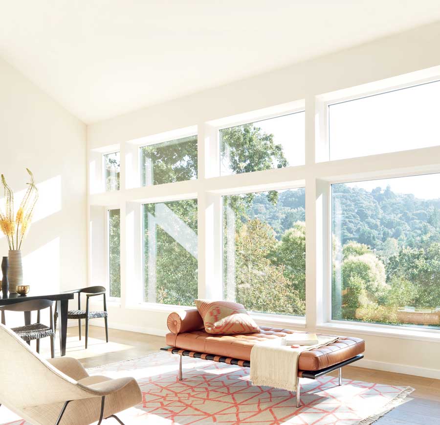 living room with bare tall windows showing sun's rays on flooring and walls