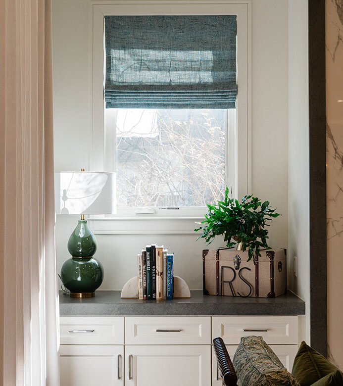 Soft blue light-filtering Roman shades on windows beside a living room fireplace