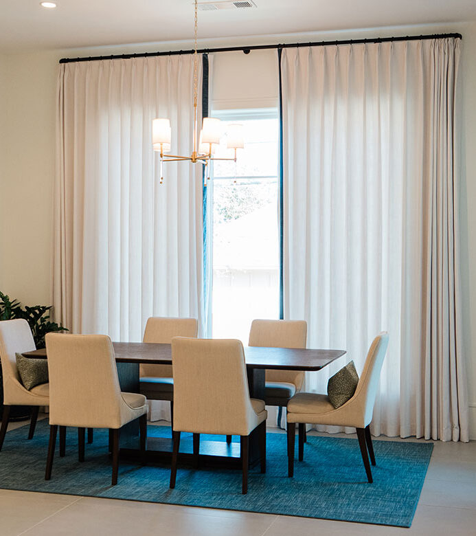 Custom neutral pinch pleat drapery with blue edge banding in a breakfast nook